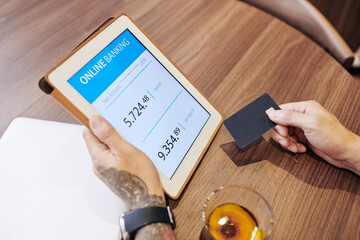 Close-up image of man transferring money from one bank to another via application on tablet computer