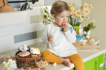 Cute little girl sitting on the kithen table and tasting easter cake decor