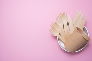 Fototapeta na wymiar Wooden and cardboard disposable tableware on a pink background. Environmentally friendly products.