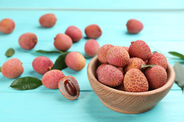 Fresh ripe lychee fruits in bowl on light blue wooden table. Space for text