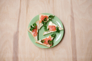 Green plate with salmon sandwiches with butter and parsley on wooden table. Buffet breakfast lunch meal. Healthy eating. Fish diet concept.