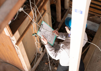 住宅　スケルトンリフォーム　解体現場で分電盤を調査するビジネスマン