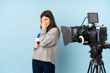 Young reporter woman holding a microphone and reporting news covering eyes and looking through...