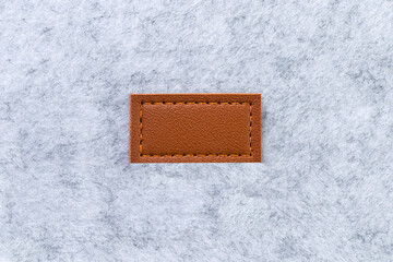Blank label made of brown genuine leather tag sewn on to light gray felt material. Copy cpase, blank