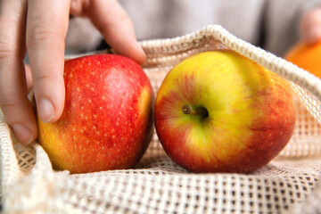 Female hand with environmentally friendly net bag for shopping groceries with Fresh fruit, Apples and oranges, eco friendly net on wooden table