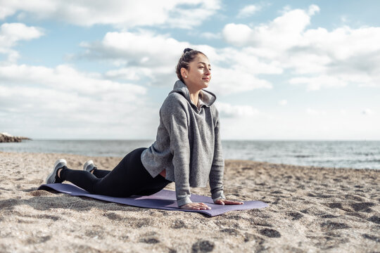 Attractive fit woman in sportswear meditates on the beach on a bright sunny day. Yoga hatha, asana, cobra pose