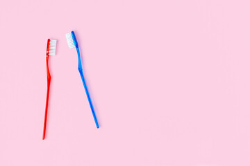 Two blue and red toothbrushes on a pink background with copy space. Men's and women's personal oral hygiene brushes, morning routine for a couple