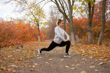 Attractive fit woman exercising outdoors. Girl doing stretching in the autumn forest