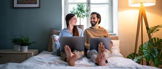 Young couple using laptops on bed indoors, home office concept.