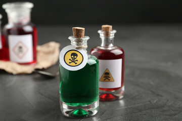 Glass bottles of poisons with warning signs on grey stone table