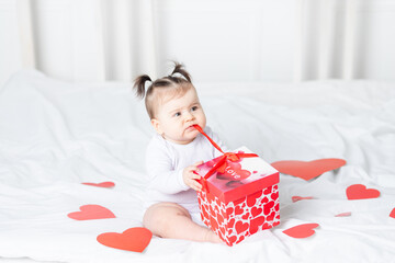 baby unties box on bed at home among hearts, Valentine's day concept