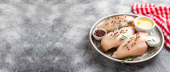 Raw uncooked chicken breasts on grey concrete background, chicken meat with ingredients for cooking. Copy space