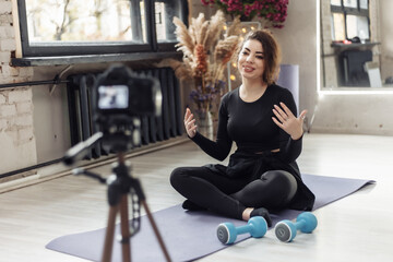 Happy smiling young woman blogger with camera on tripod recording fitness blog. Fitness, sport and...
