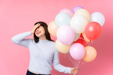 Young Ukrainian teenager girl holding lots of balloons over isolated pink background laughing