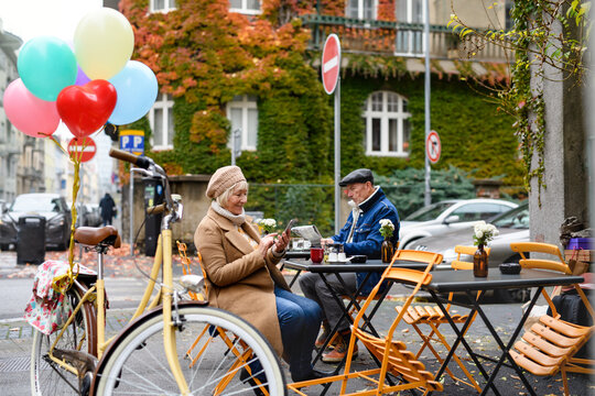 Senior people sitting in outdoor cafe in city, using smartphone.