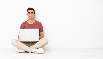 Teenager man sitting on the flor with his laptop laughing