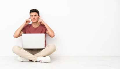 Teenager man sitting on the flor with his laptop having doubts and thinking