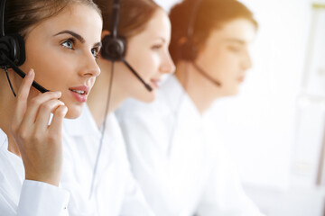 Call center. Beautiful young woman using headset and computer to help customers in sunny office. Business concept