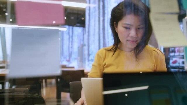 attractive freelance asian female creative person wear casual yellow cloth working with laptop at share area coworking space new lifestyle with thoughful and freshness emotion blur office background