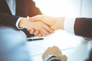 Business people shaking hands finishing up meeting or negotiation in sunny office. Business handshake and partnership concepts