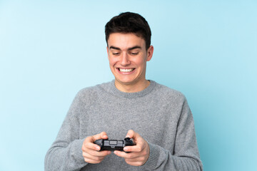 Teenager caucasian man playing with a video game controller isolated on blue background