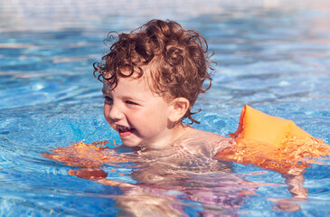 Young Boy In Outdoor Pool On Summer Vacation Learning To Swim With Inflatable Armbands