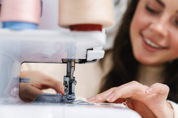 Nice happy girl seamstress smiling while working with sewing machine