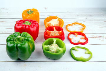 Red, orange and green bell peppers on top of wooden table put in group of whole, half, and slices