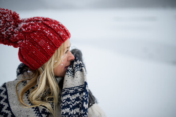 Portrait of senior woman with hat and mittens outdoors standing in snowy nature.