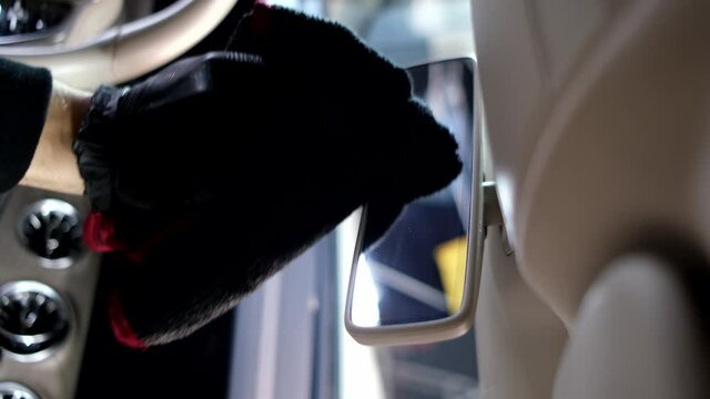 Vertical video. Car detailing - the man holds the microfiber in hand and polishes the rearview mirror. Selective focus.