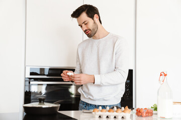 Pleased young man using earphones while cooking scrambled eggs