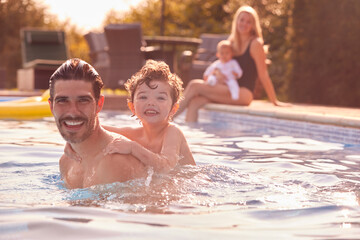 Obraz premium Portrait Of Father And Son Playing In Outdoor Pool On Vacation As Mother And Baby Watch From Side