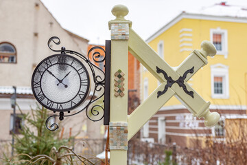 Round glass clock with black arrows on a city street