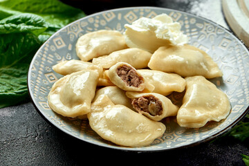 Ukrainian or Polish traditional dish - Pierogi or Varenyky (dumplings) stuffed with meat and sour cream. dark background. Close up, selective focus
