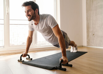 Joyful athletic man doing exercise with push-up stops while working out - obrazy, fototapety, plakaty