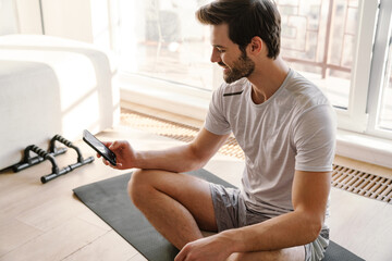 Happy athletic handsome man using mobile phone while working out
