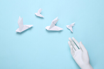 Origami pigeons and hand on blue background. Peace symbol