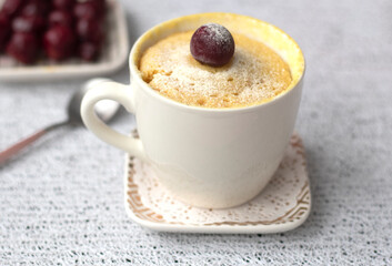 vanilla cupcake with cherries in a mug. Easy microwave cooking concept. The muffin is decorated with fresh cherries. White cup on a light background. Delicious sweet dessert. High quality photo