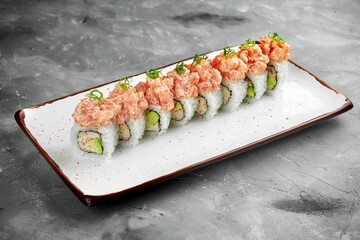 Japanese sushi roll with crab, avocado and spicy salmon in a white plate on a gray background