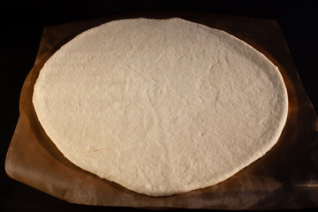 Raw dough for pizza on parchment paper on black background