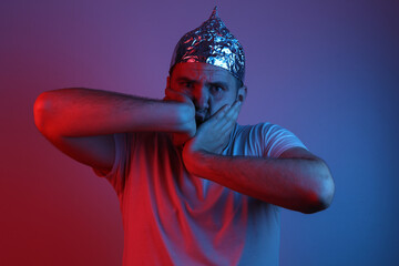 Young man withfoil hat in red-blue neon light. Conspiracy