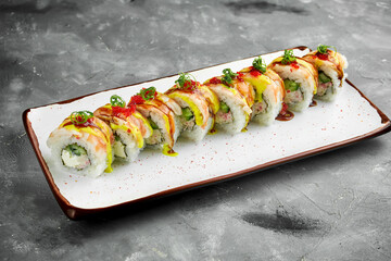 Japanese sushi roll with shrimp, cucumber, cream cheese and unagi sauce, tobiko caviar in a white plate on a gray background. Roll drenched in peach sauce