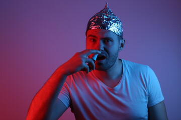 Bearded man in foil hat puffs his nose with nasal spray in red-blue neon light.