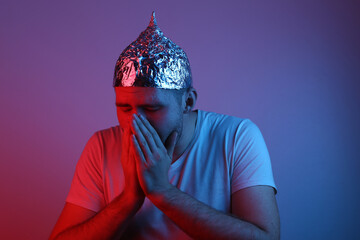 A bearded man in a foil hat coughs in the red-blue neon light. Conspiracy. Conspiracy theory