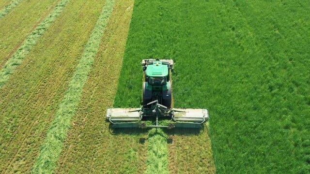 Tractor In Agricultural Field Mowing Fresh Green Grass For Hay Aerial View