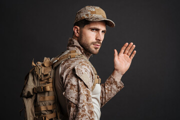 Fototapeta premium Confident masculine military man waving hand while posing with backpack