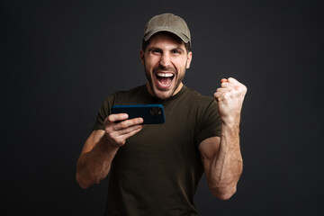 Excited masculine military man playing online game on mobile phone