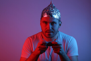 Bearded Man in foil hat with gempad playing video game in a red blue neon light.