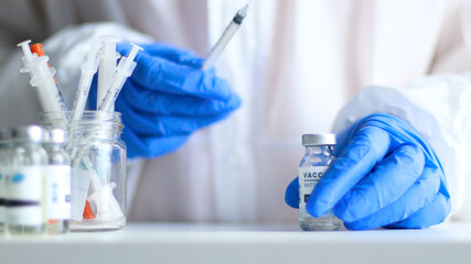 Nurse or doctor in medical protective uniform and latex rubber gloves holding syringe with vaccine while preparing for work during coronavirus, flu or measles pandemic for poster, web banner, article