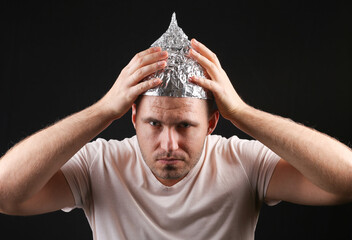 Crazy man in aluminum foil cap on black background